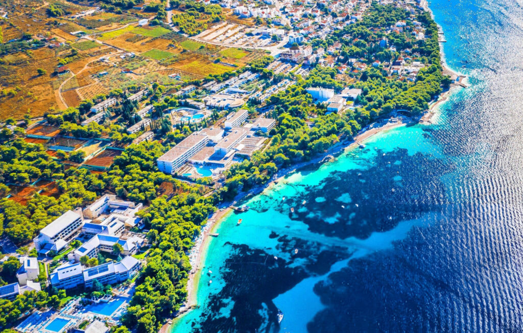 A picturesque view of Bol town, Croatia, featuring traditional stone buildings, narrow streets, and vibrant flowers against a backdrop of the Adriatic Sea