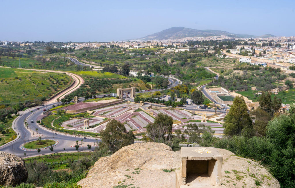 A view of the city of Fes, Morocco, featuring a road winding through the urban landscape with patches of sand visible in the surrounding area