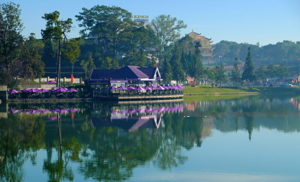 A serene view of Xuan Huong Lake in Dalat, Vietnam, with calm waters reflecting the surrounding trees and mountains