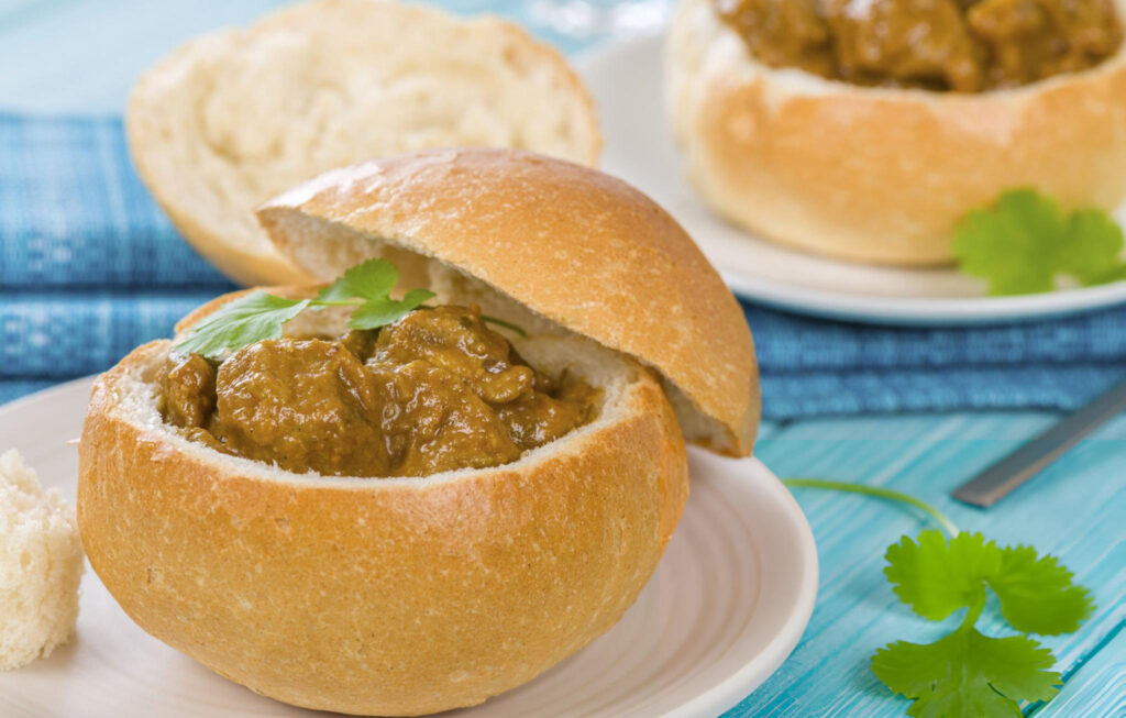 A close-up of a traditional Durban bunny chow, featuring a hollowed-out loaf of bread filled with spicy curry