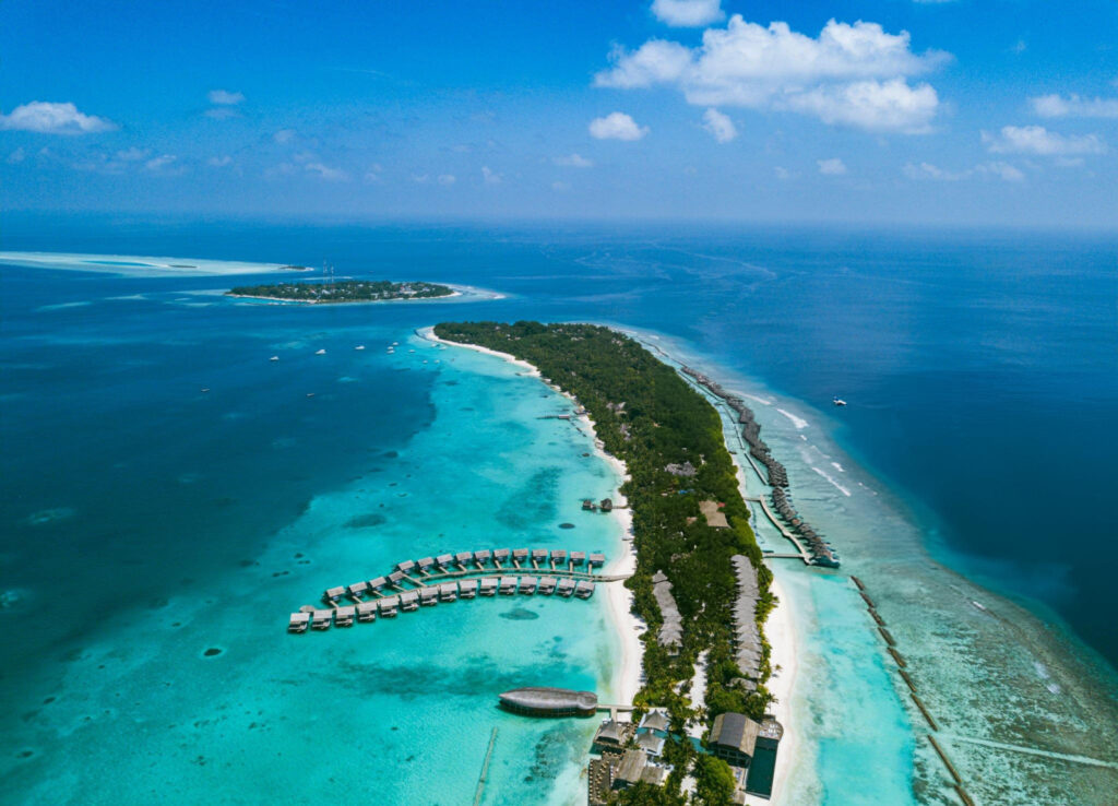 Aerial view of Dhangethi Island in the Maldives, showcasing white sandy beaches, lush greenery, and turquoise waters surrounded by coral reefs