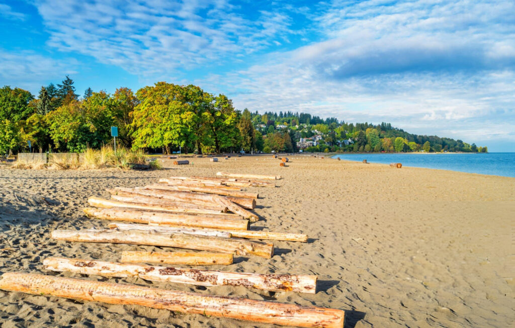 A scenic beach in Vancouver, Canada, with golden sand, clear blue water, and coastal mountains in the background