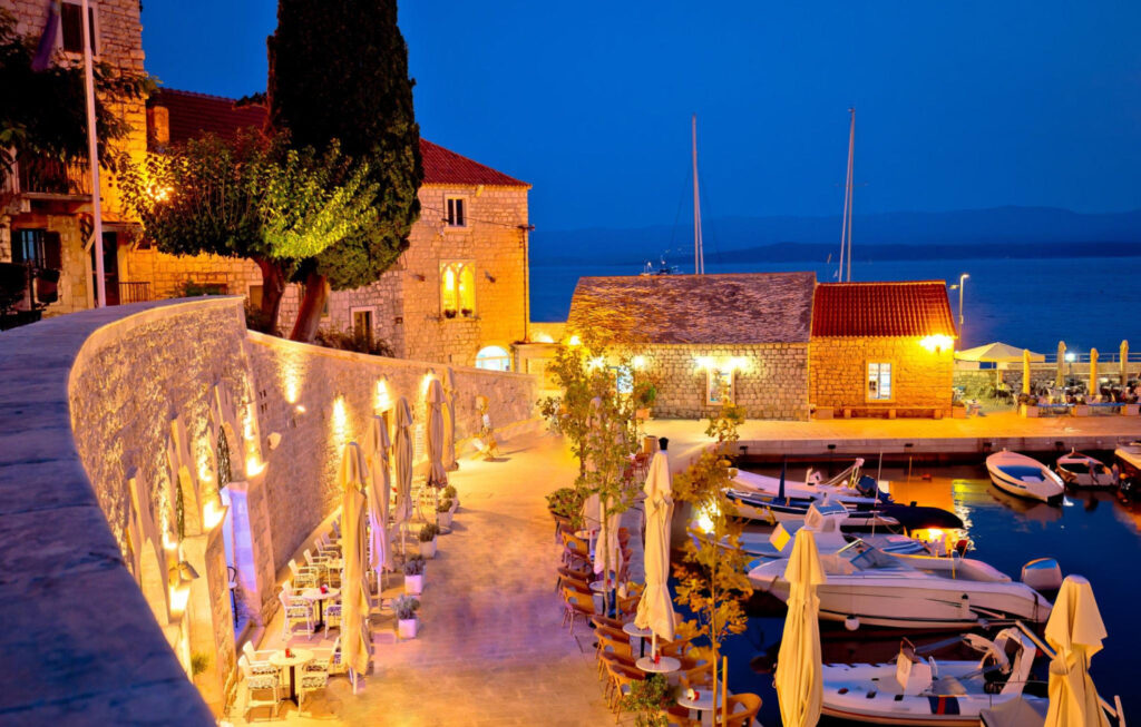 A modern hotel exterior in Bol, Croatia, featuring a pool, lush gardens, and balconies overlooking the sea