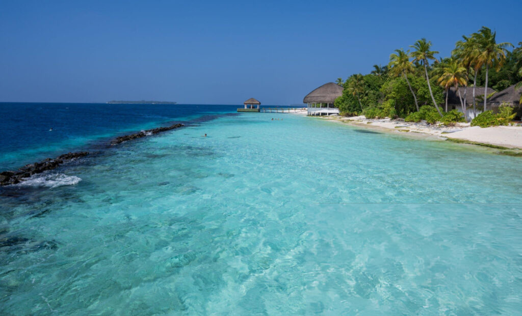 A stunning view from the water toward Dhangethi Island, Maldives, showcasing crystal-clear turquoise waters, white sandy beaches, and lush green palm trees