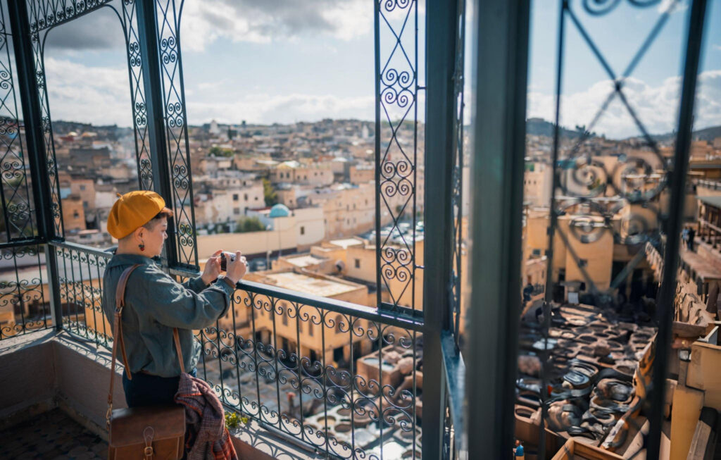 A man overlooking the city of Fes from a higher vantage point, with a panoramic view of the urban landscape and rooftops below