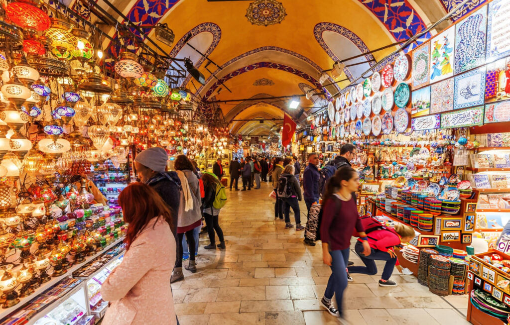 A bustling scene inside the Grand Bazaar in Istanbul, Turkey, with a vibrant array of shops and stalls displaying colorful textiles, jewelry, and traditional goods, and visitors exploring the historic marketplace