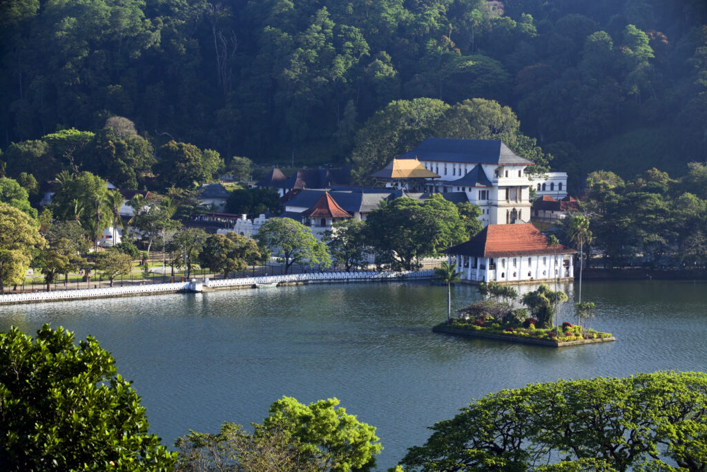 A breathtaking landscape view of Kandy Lake, surrounded by lush greenery and scenic hills, with reflections of the sky on the water's surface