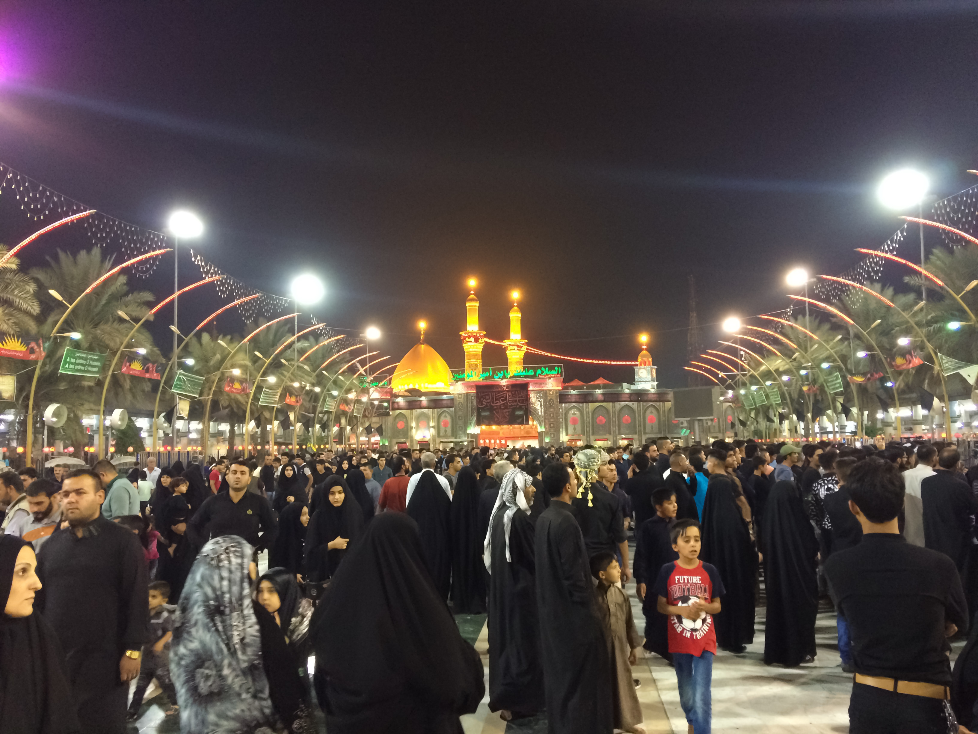 Imam Hussain Shrine in Karbala, Iraq, featuring a golden dome and minarets surrounded by pilgrims and vibrant decorations