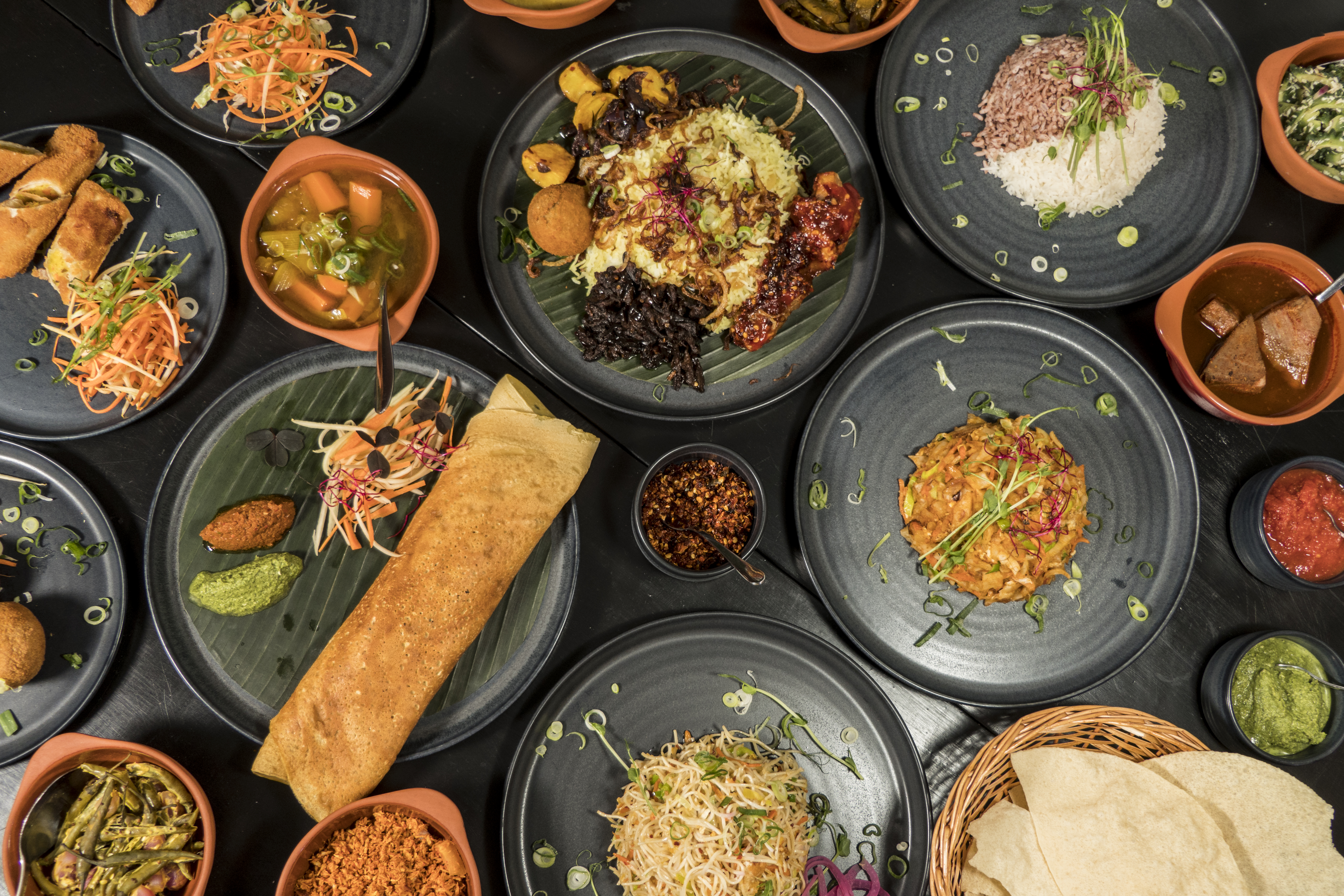 A collection of colorful plates showcasing various traditional Sri Lankan dishes, including rice, curries, and fresh vegetables, arranged beautifully