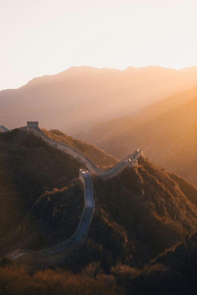 An ancient stone section of the Great Wall of China, stretching over green rolling hills and disappearing into the misty horizon