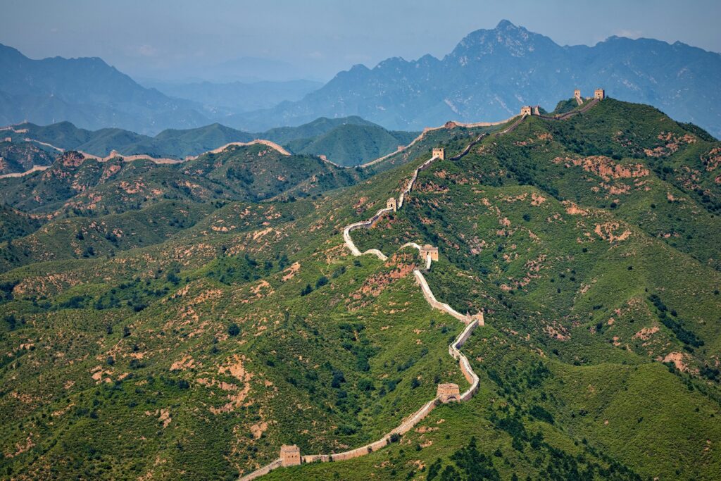 A panoramic view of the Great Wall of China winding across rugged mountains under a bright blue sky