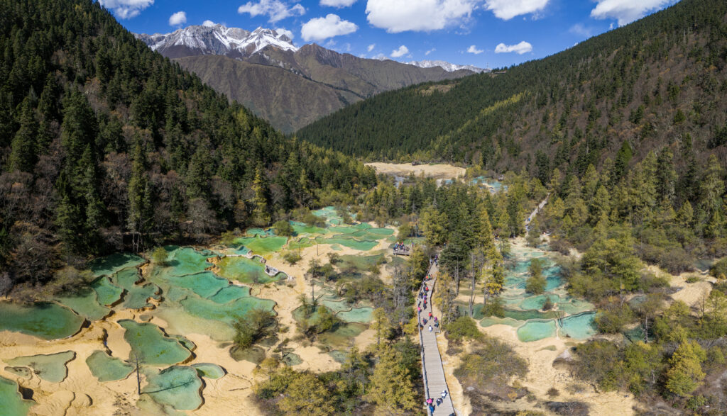 Stunning view of Huanglong Valley in China, showcasing colorful travertine pools and lush greenery surrounded by mountains