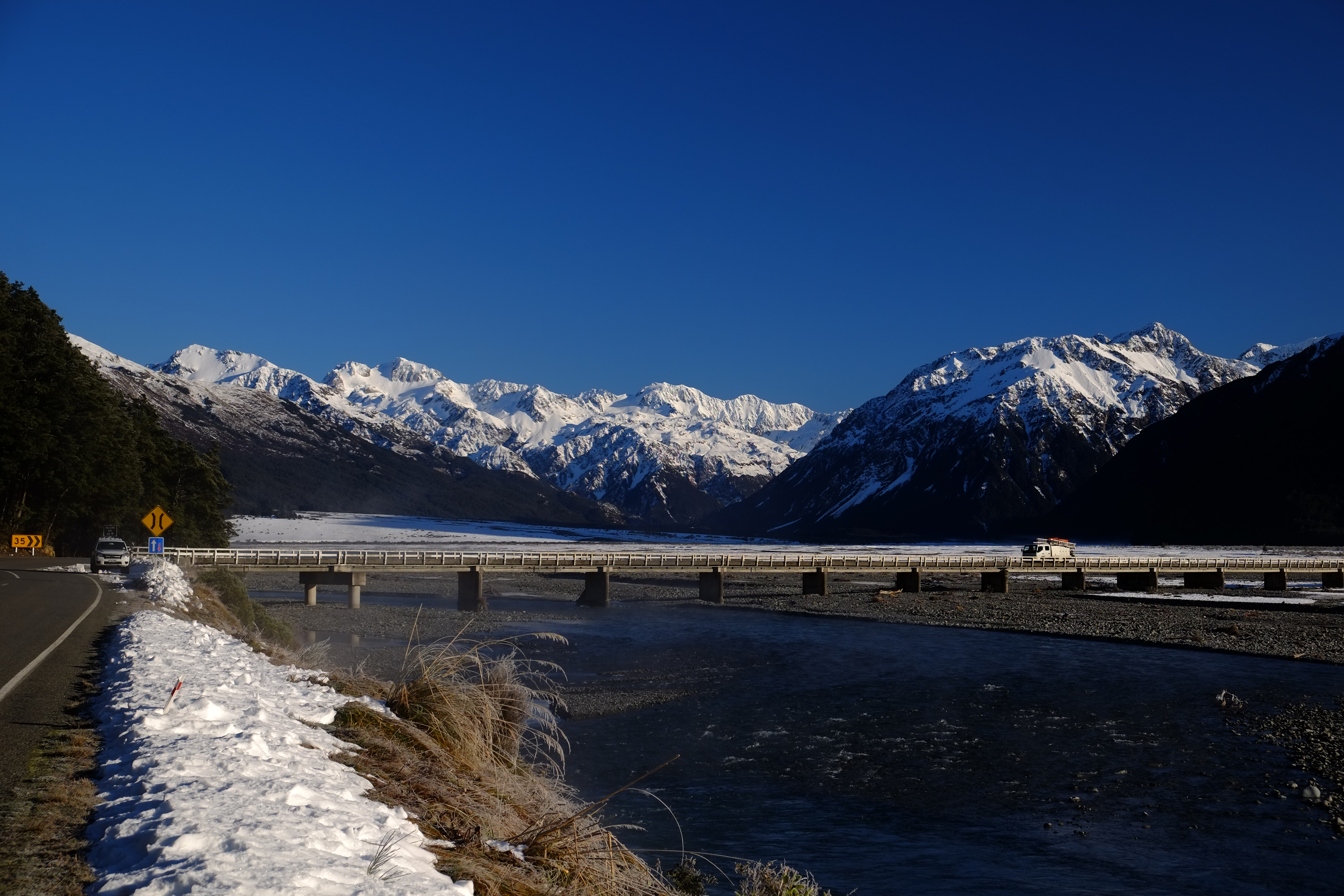 Snow-covered Waimakariri River in winter with icy blue waters winding through frosty landscapes and snow-capped Southern Alps in the background