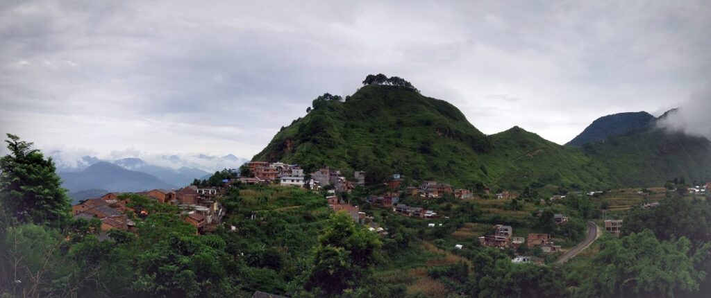 Lush green hillside with scattered houses and a backdrop of mountains during sunset