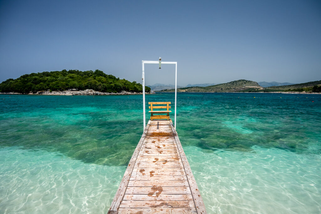 Ksamil beach with golden sand, turquoise waters, and small islands in the distance under a clear blue sky