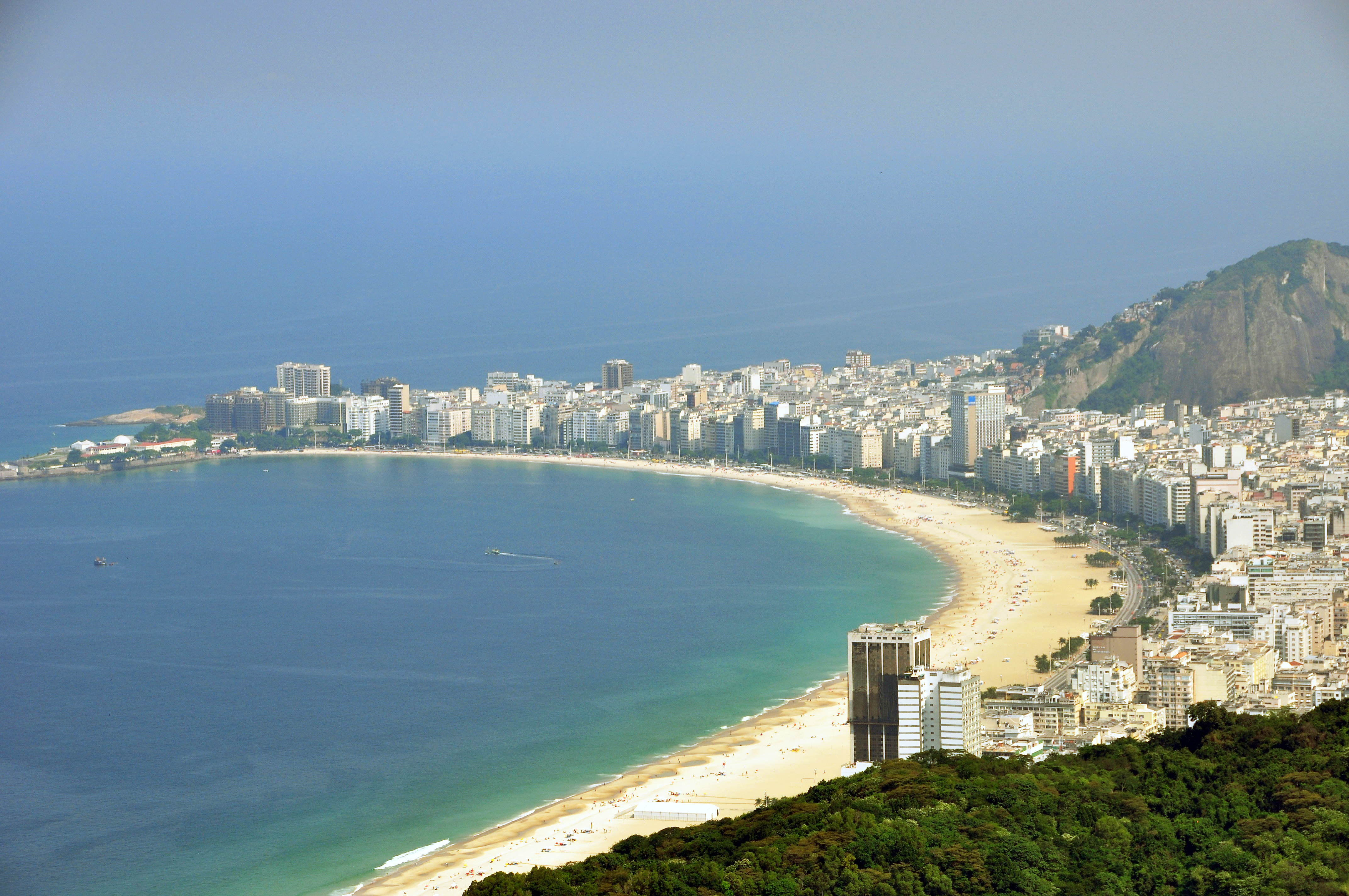 A scenic view of Copacabana Beach in Rio de Janeiro, with its iconic curved shoreline, bustling beachgoers, and the city skyline in the background