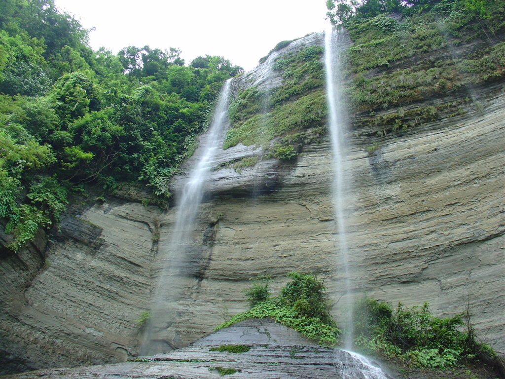 Shuvolong Waterfall cascading down rocky cliffs surrounded by greenery in Rangamati, Bangladesh.