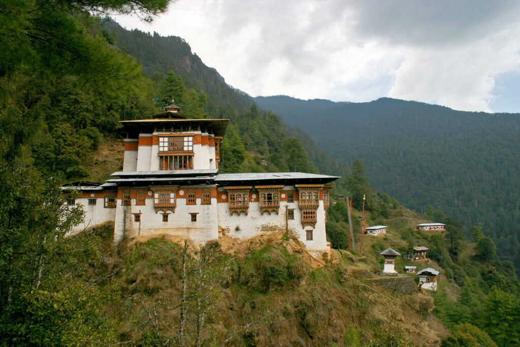 A scenic view of Tango Monastery, showcasing its traditional Bhutanese architecture set against lush green hills and a clear blue sky