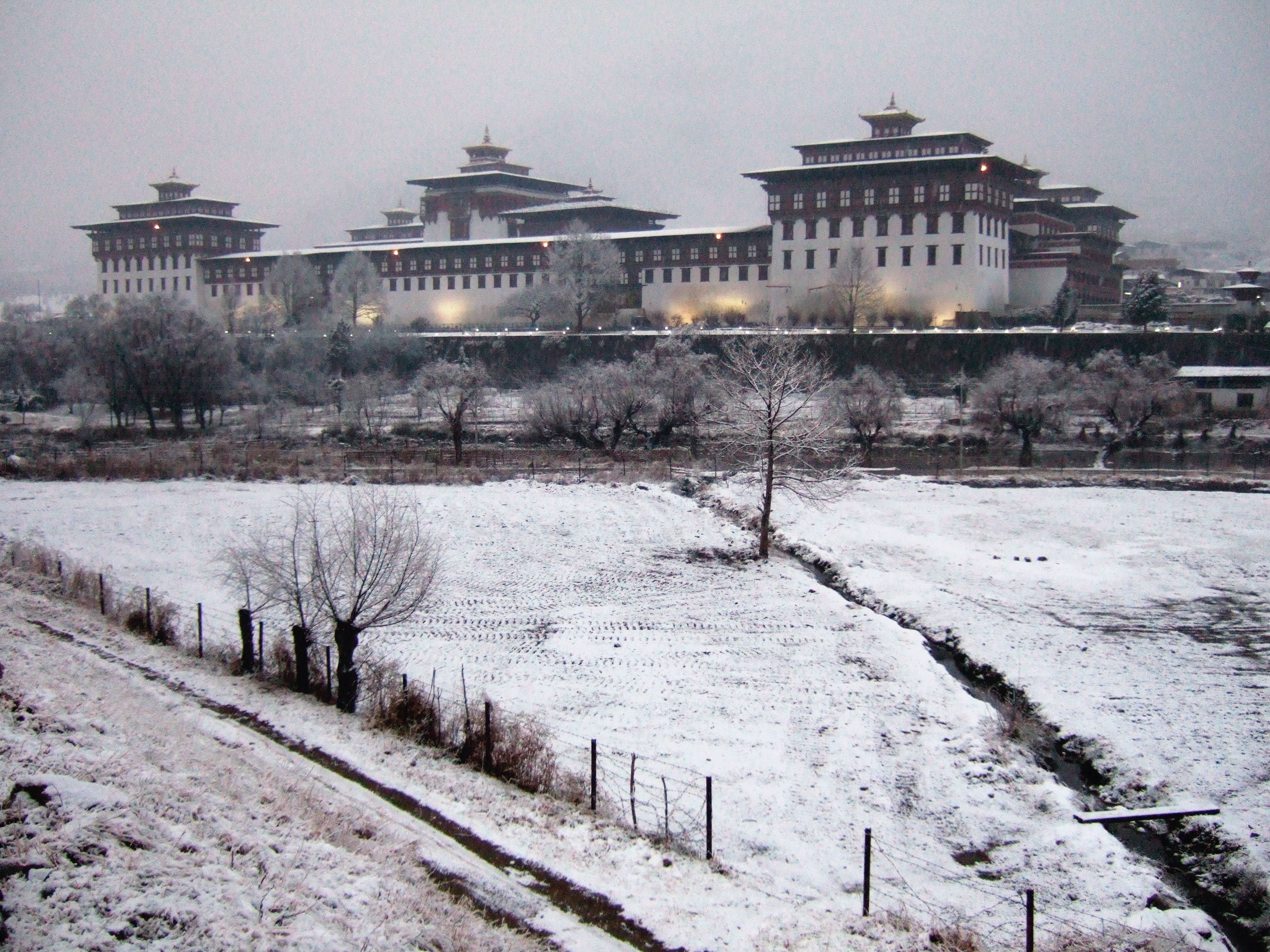 A majestic view of Tashichödzong in Thimphu, Bhutan, featuring its ornate architecture, golden roofs, and lush gardens with the Himalayas in the background