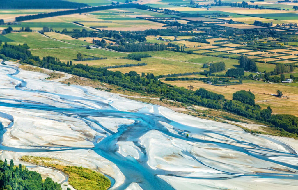 Aerial view of Waimakariri River showcasing its braided channels winding through the Canterbury Plains with distant mountains under a clear sky