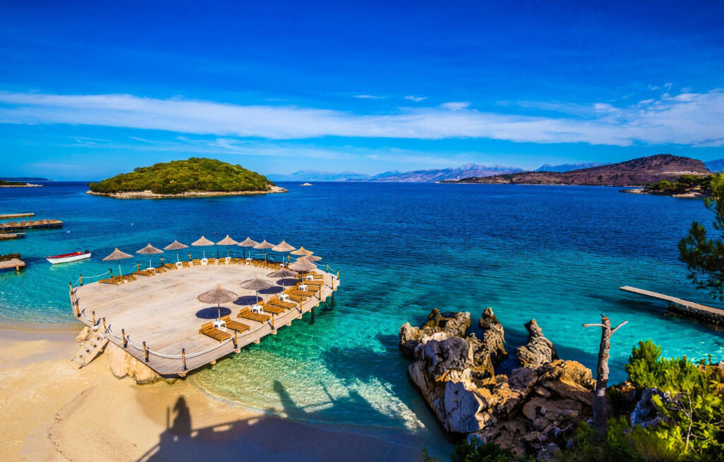 A serene spot by the shore in Ksamil, with empty chairs facing the calm turquoise water and distant islands