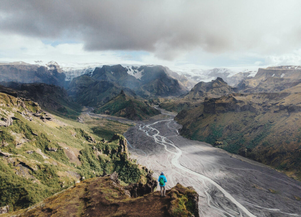 A female hiker standing on a trail in Thórsmörk Valley, surrounded by lush greenery, mountains, and glacial rivers