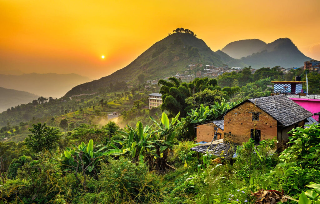 Sunset view over a lush green hillside with houses, framed by mountains in the background