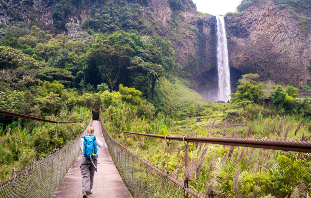 A girl crossing a bridge with a waterfall in the background near Baños, Ecuador
