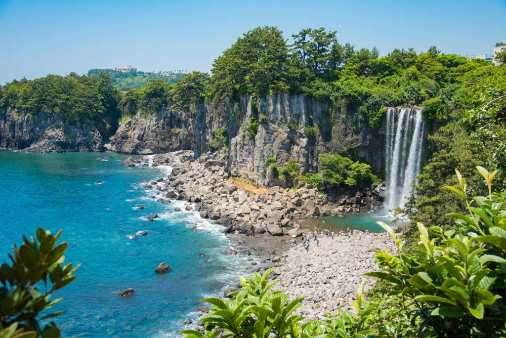 A stunning view of Jeongbang Waterfall cascading into the ocean, surrounded by lush greenery in Jeju-si, South Korea