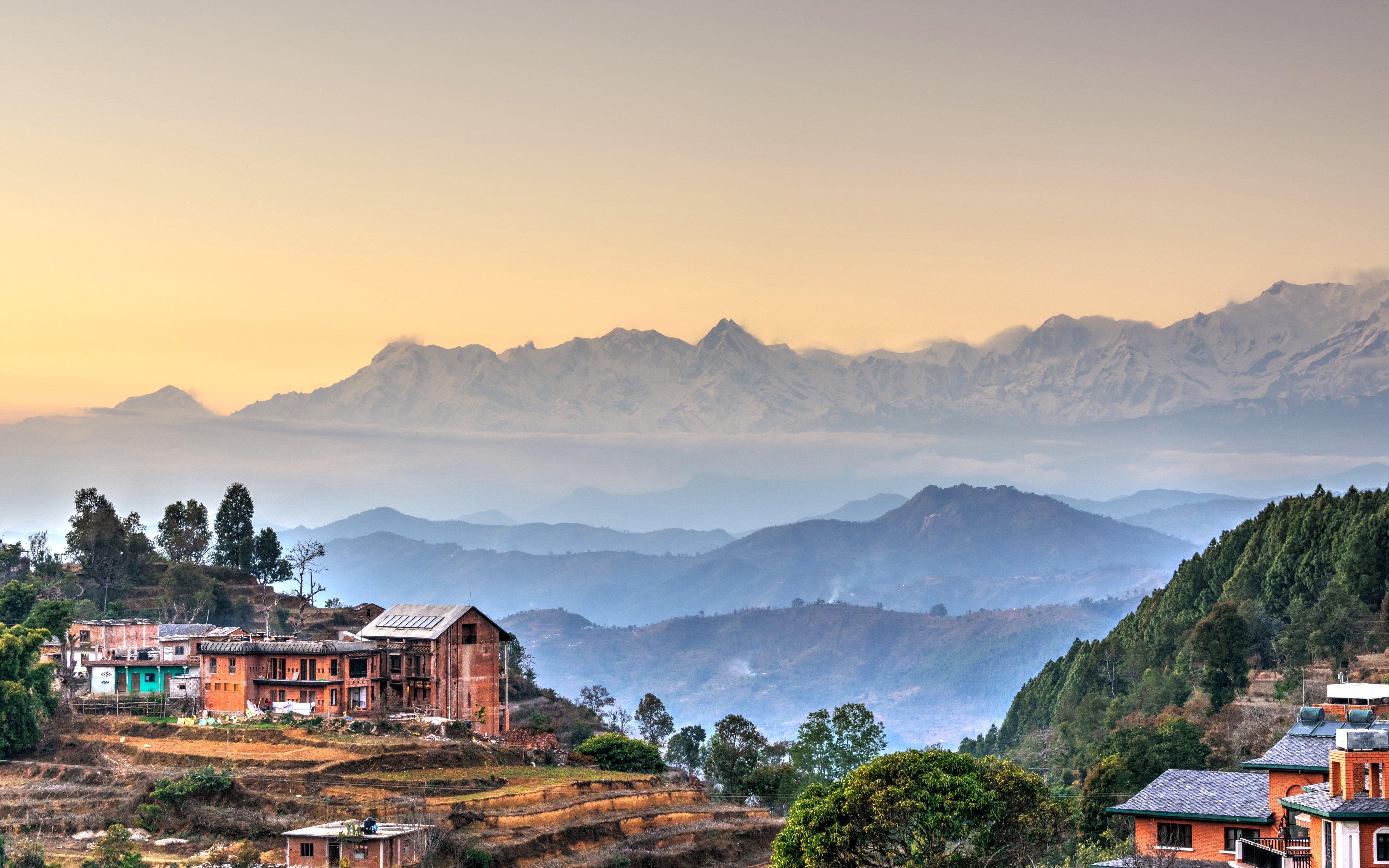 Sunset view over a lush green hillside with houses, framed by mountains in the background