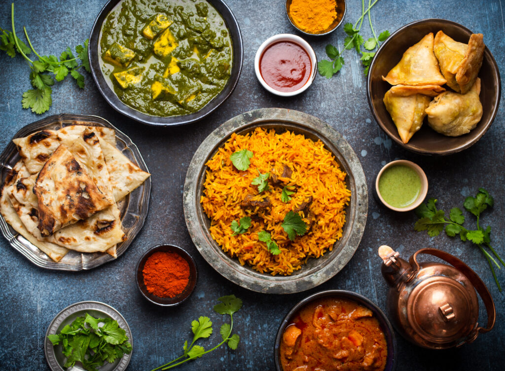 An array of traditional Indian dishes including biryani, naan bread, samosas, and various sauces, beautifully presented on a table