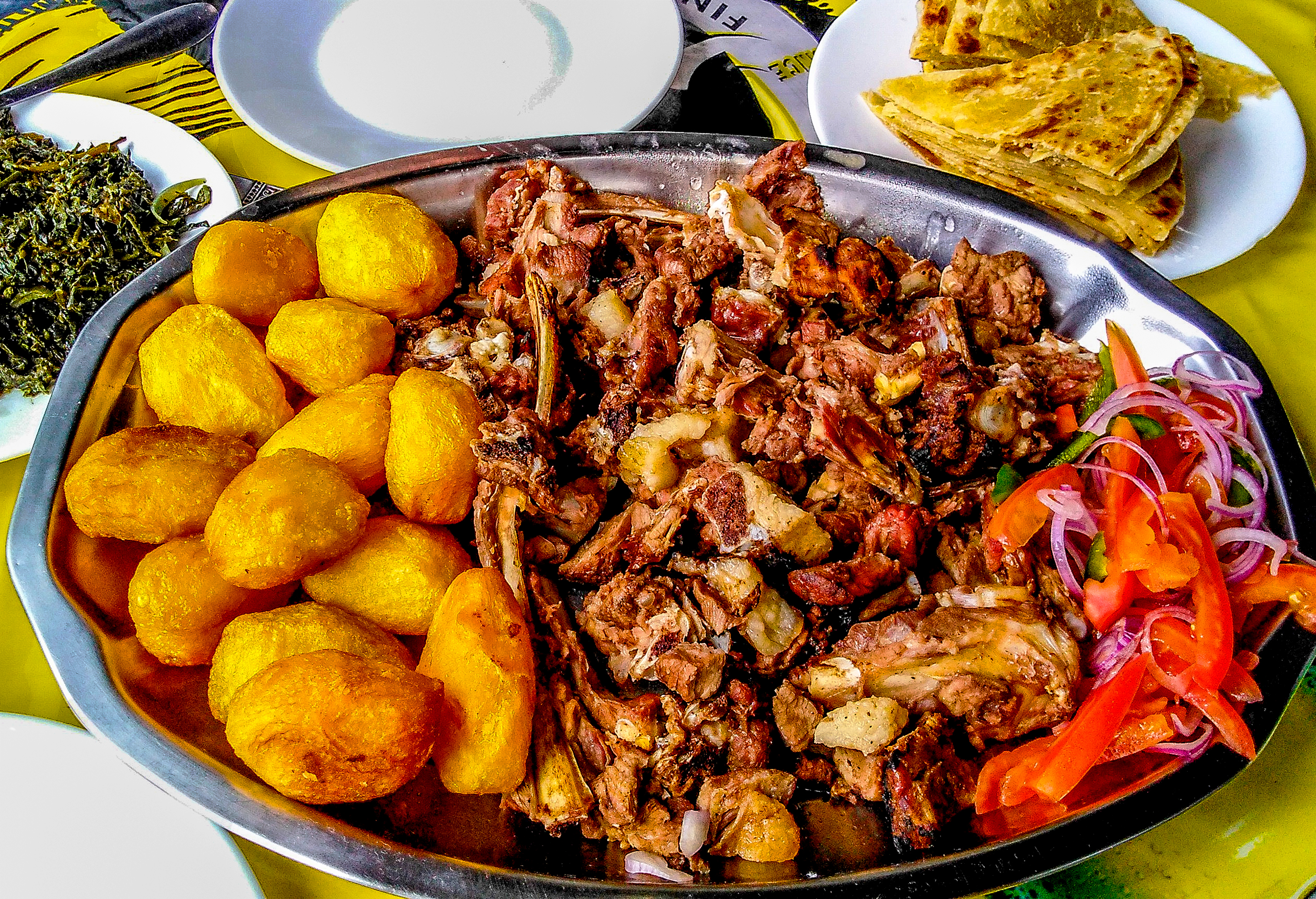 A table filled with traditional Kenyan dishes like Nyama Choma, Ugali, Sukuma Wiki, and Chapati in a Nairobi restaurant.