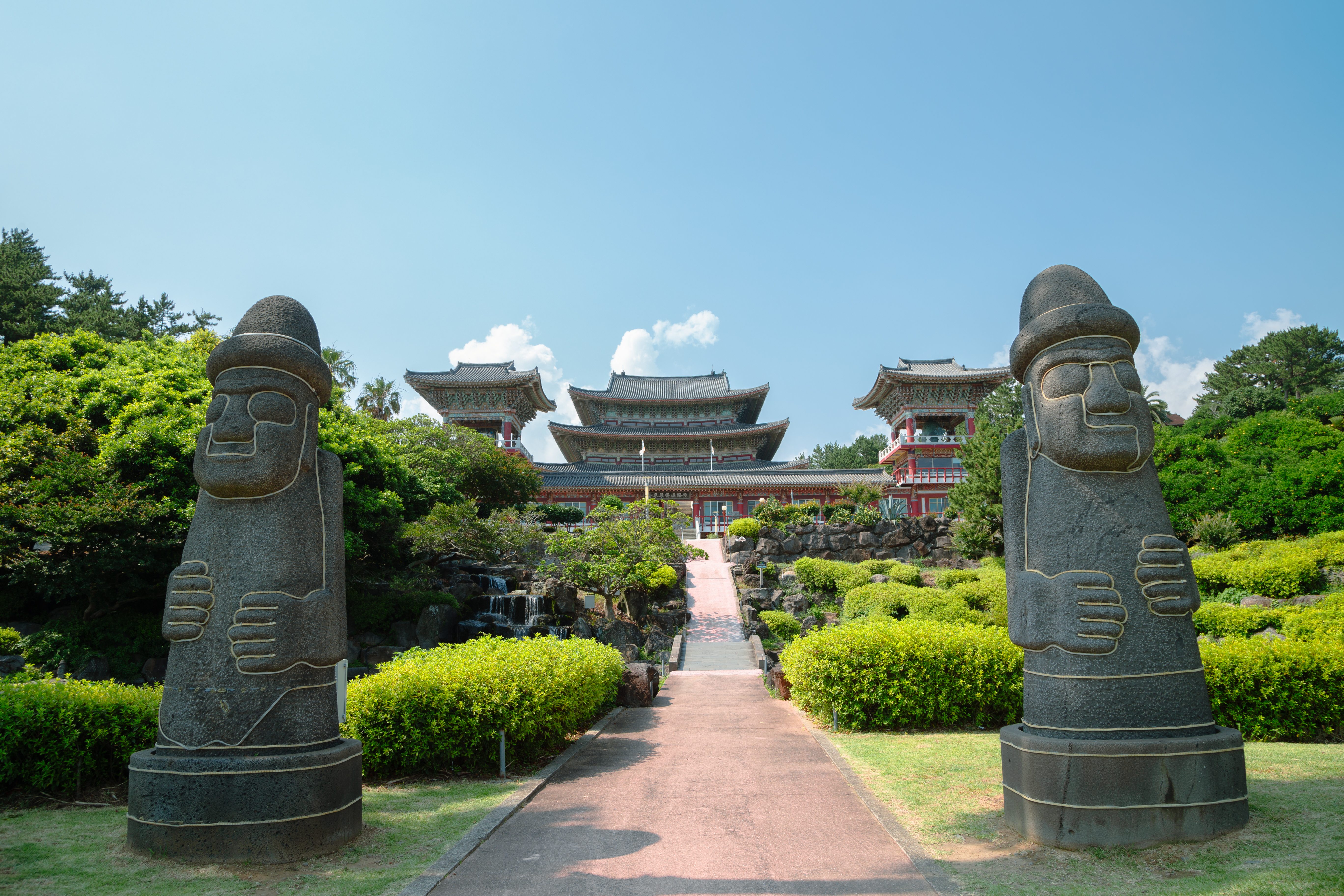 A serene view of a traditional Korean temple surrounded by lush trees and mountains in Jeju-si, South Korea
