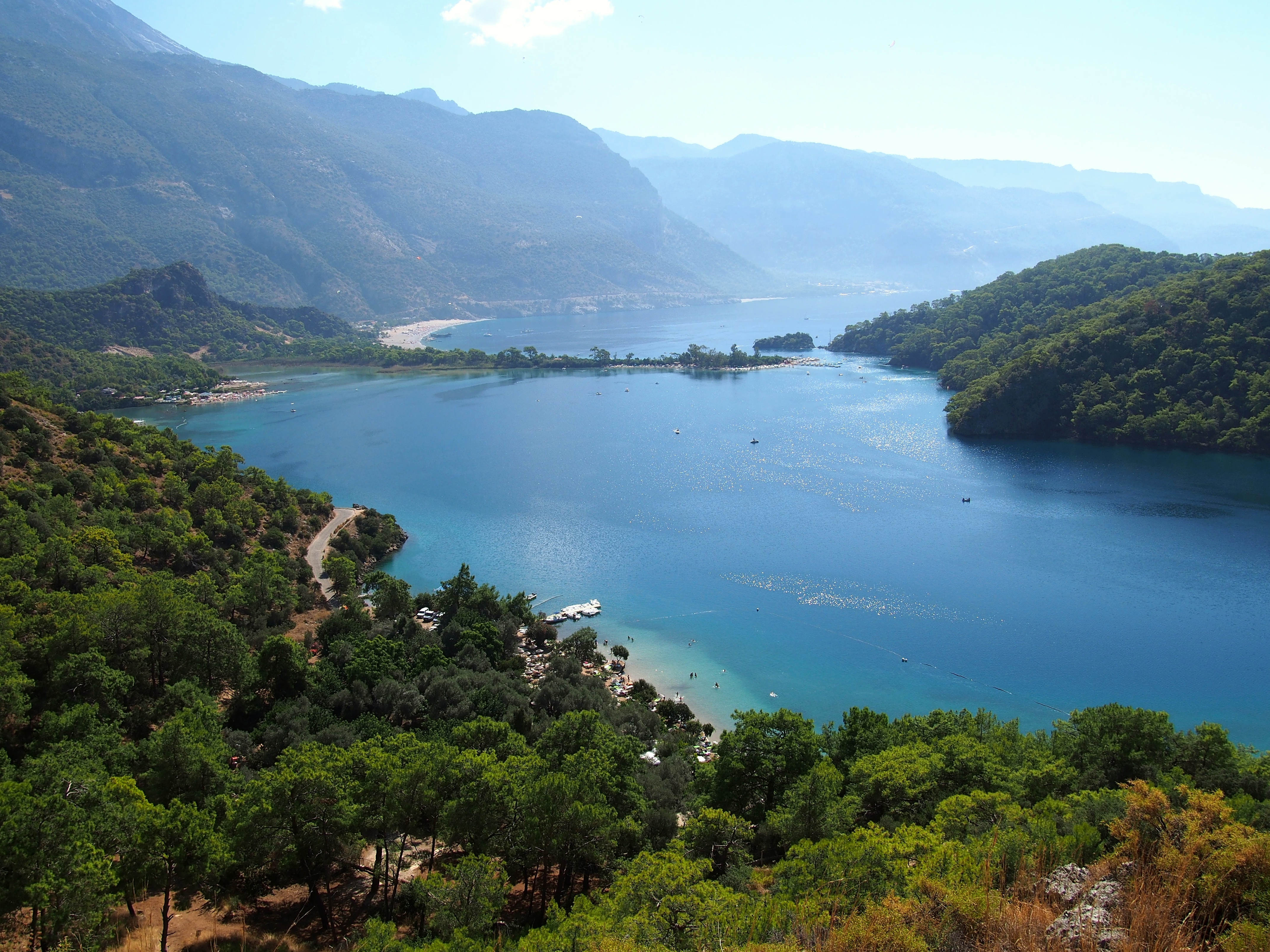 Overview of Ölüdeniz Beach in Turkey, with turquoise waters, a sandy shoreline, the iconic Blue Lagoon, and surrounding lush green hills