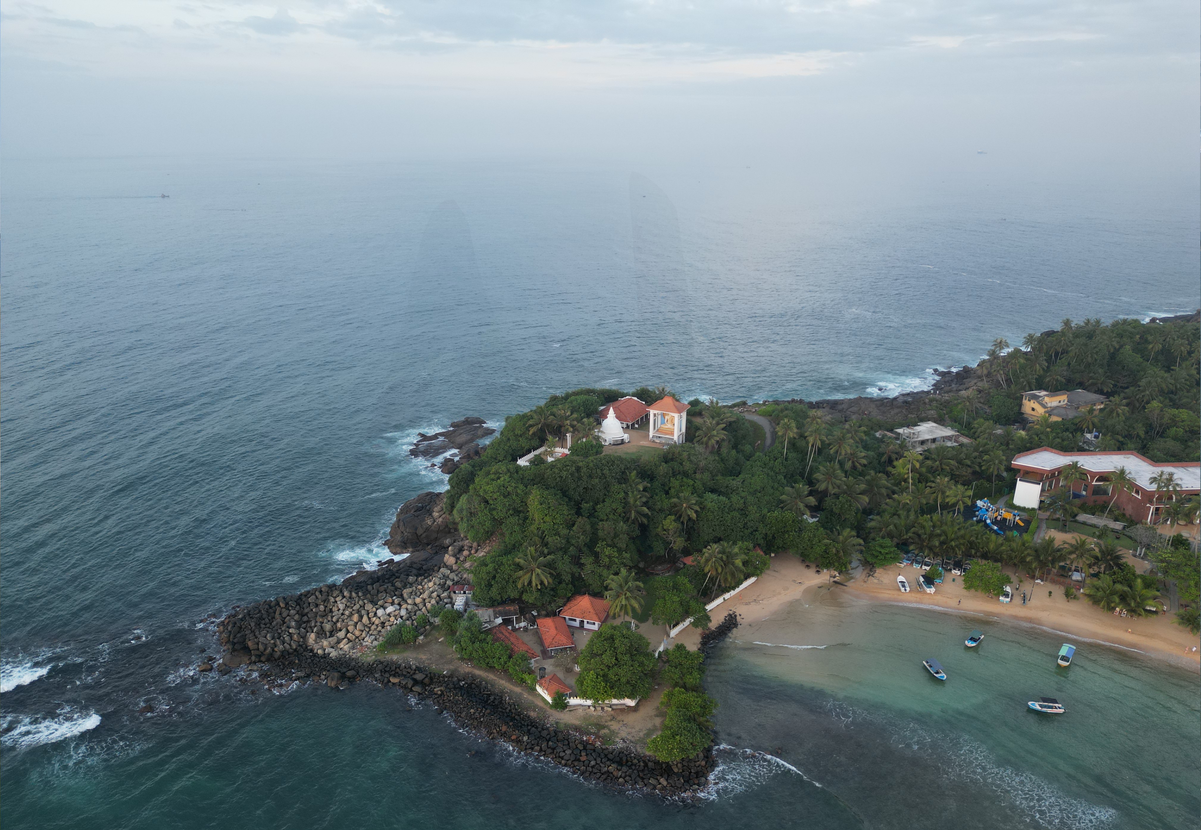 An aerial view of Unawatuna Beach in Sri Lanka, showcasing its crescent-shaped shoreline, turquoise waters, and lush green surroundings.