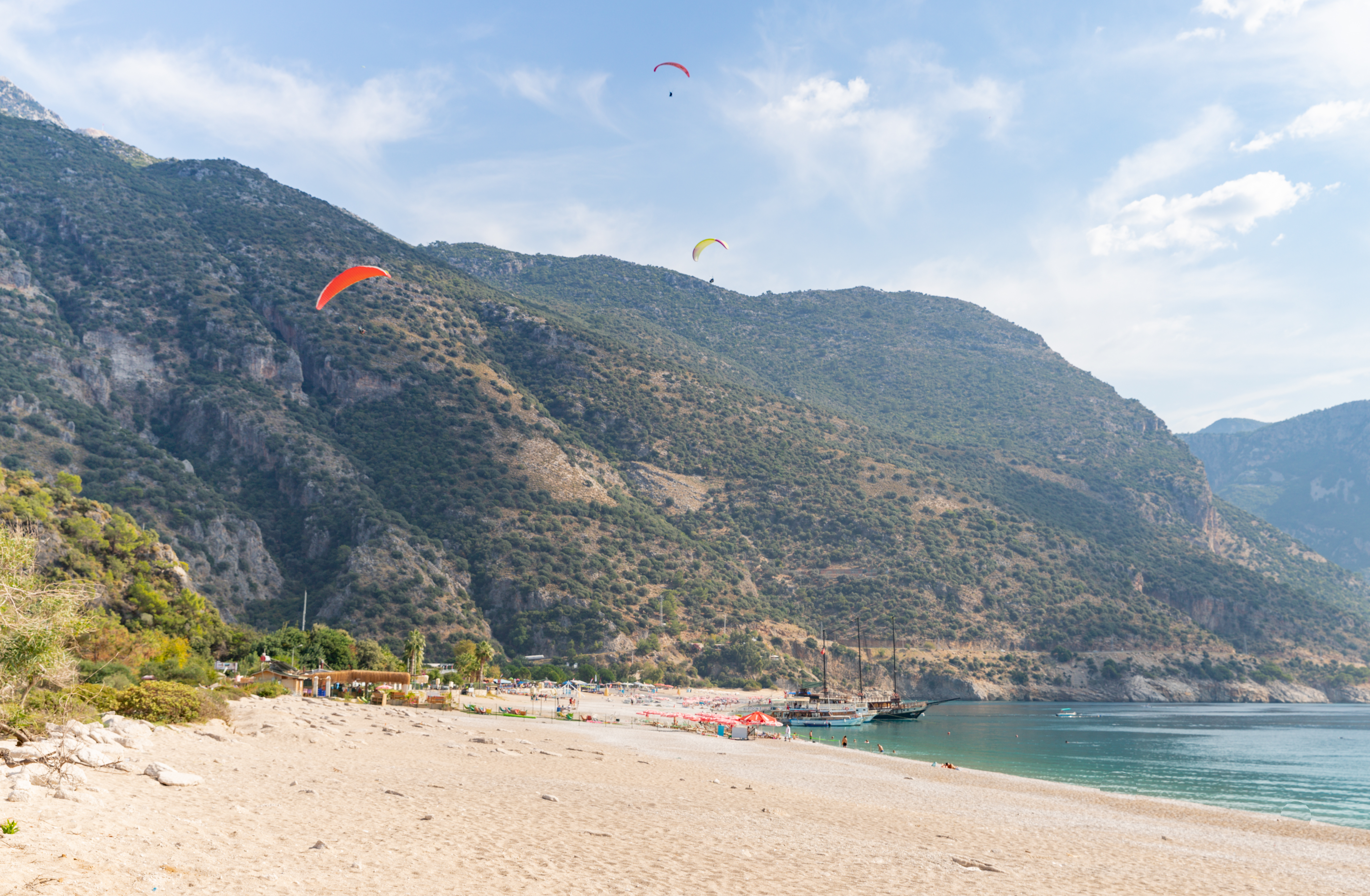 A paraglider soaring over Ölüdeniz Beach in Turkey, with stunning views of the Blue Lagoon and turquoise waters below