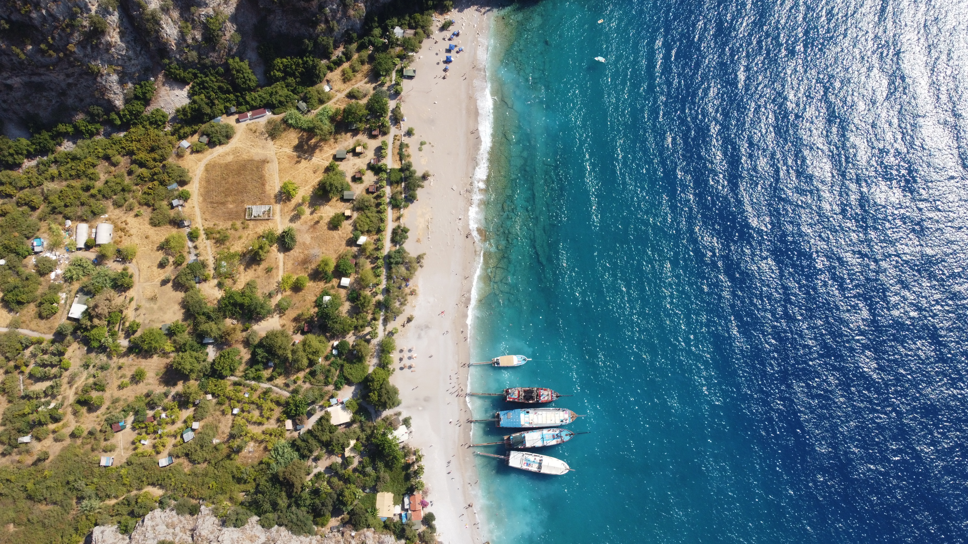 The sandy beach of Butterfly Valley with calm turquoise waters, surrounded by towering cliffs and vibrant greenery