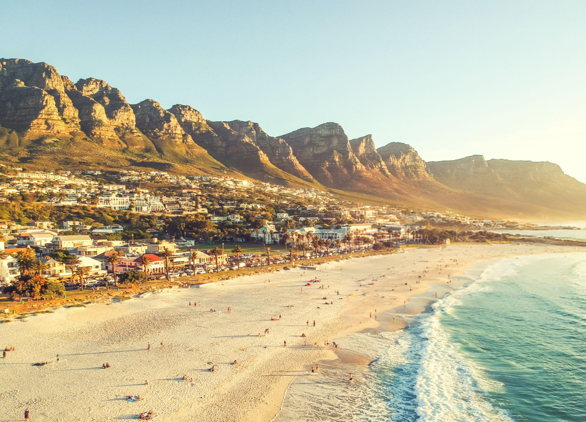 Aerial view of Camps Bay Beach with turquoise waters, white sand, and the Twelve Apostles mountain range in Cape Town, South Africa