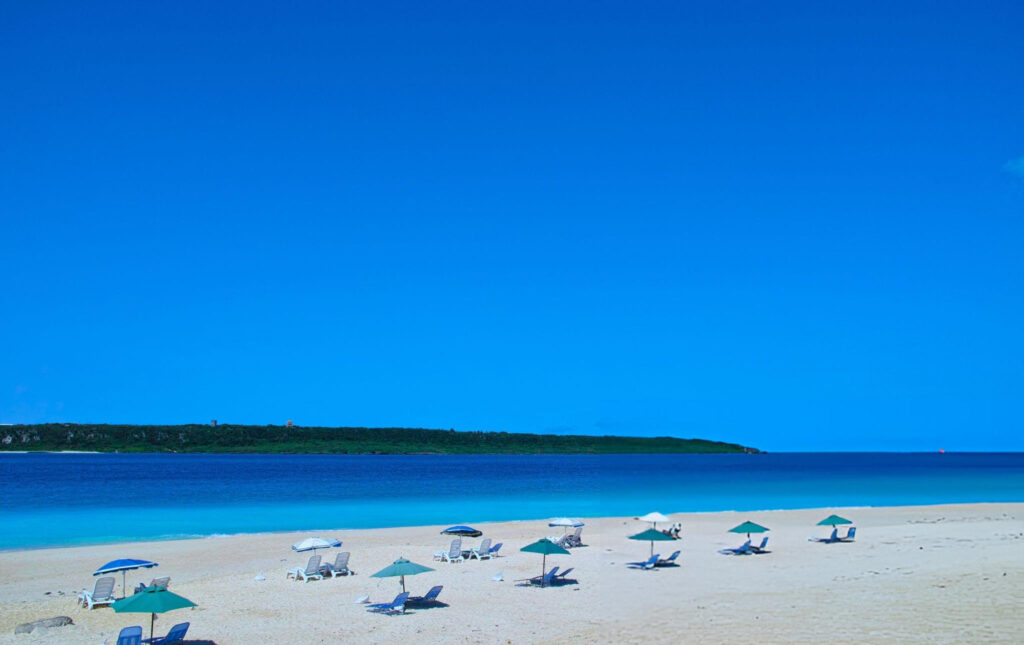 Relaxing spot on Yonaha Maehama Beach with soft white sand, a beach umbrella, and a clear view of the turquoise sea, Okinawa, Japan