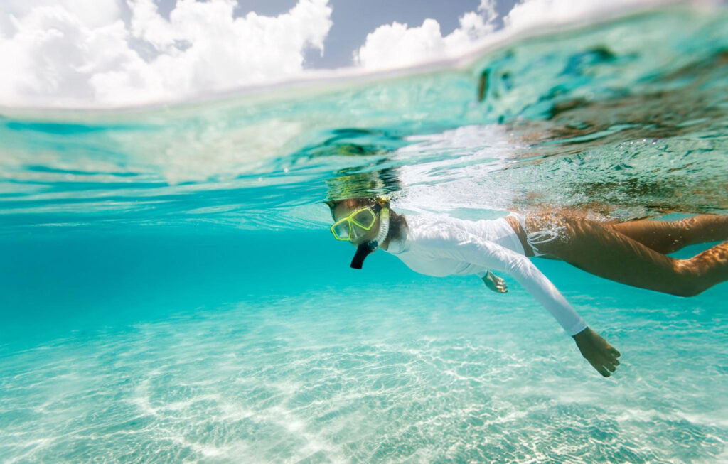 Woman snorkeling in the clear turquoise waters of Yonaha Maehama Beach, surrounded by vibrant marine life, Okinawa, Japan