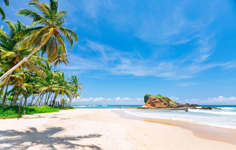 A breathtaking view of Unawatuna Beach in Sri Lanka, featuring golden sands, turquoise waters, and lush green palm trees under a vibrant sky.