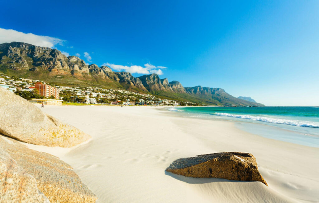 Vibrant sunset over Camps Bay Beach with silhouetted palm trees and waves lapping the shore, creating a picturesque evening scene in Cape Town, South Africa