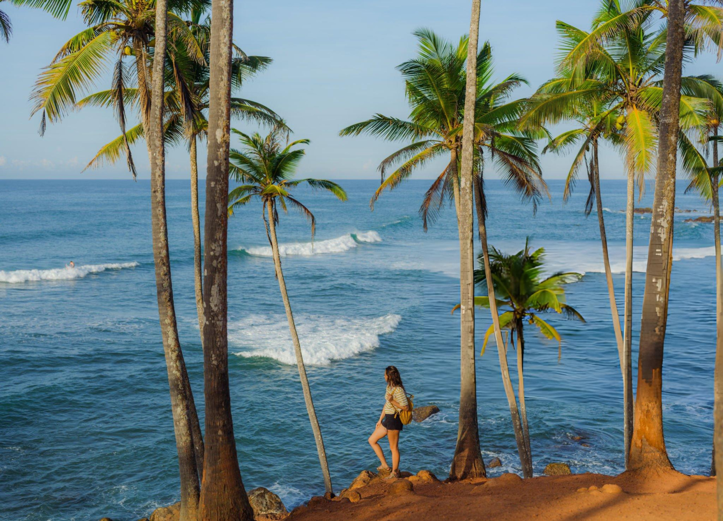 A serene beach scene with golden sands, turquoise waters, and lush green palm trees under a bright blue sky.