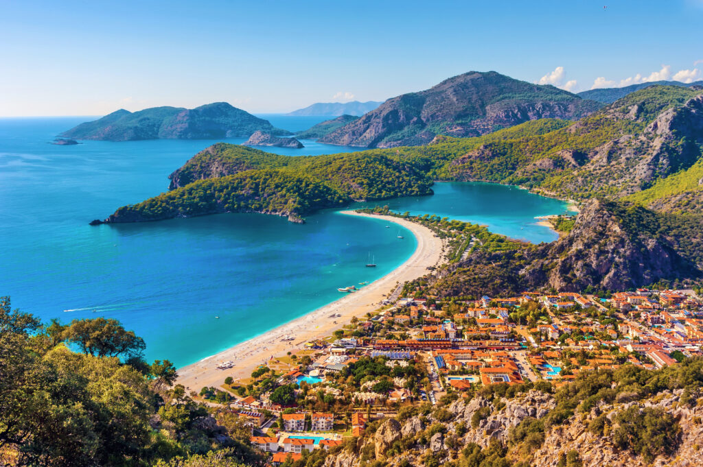 Aerial view of Ölüdeniz Beach in Turkey, with turquoise waters, a sandy shore, and the lush green surroundings of the Blue Lagoon