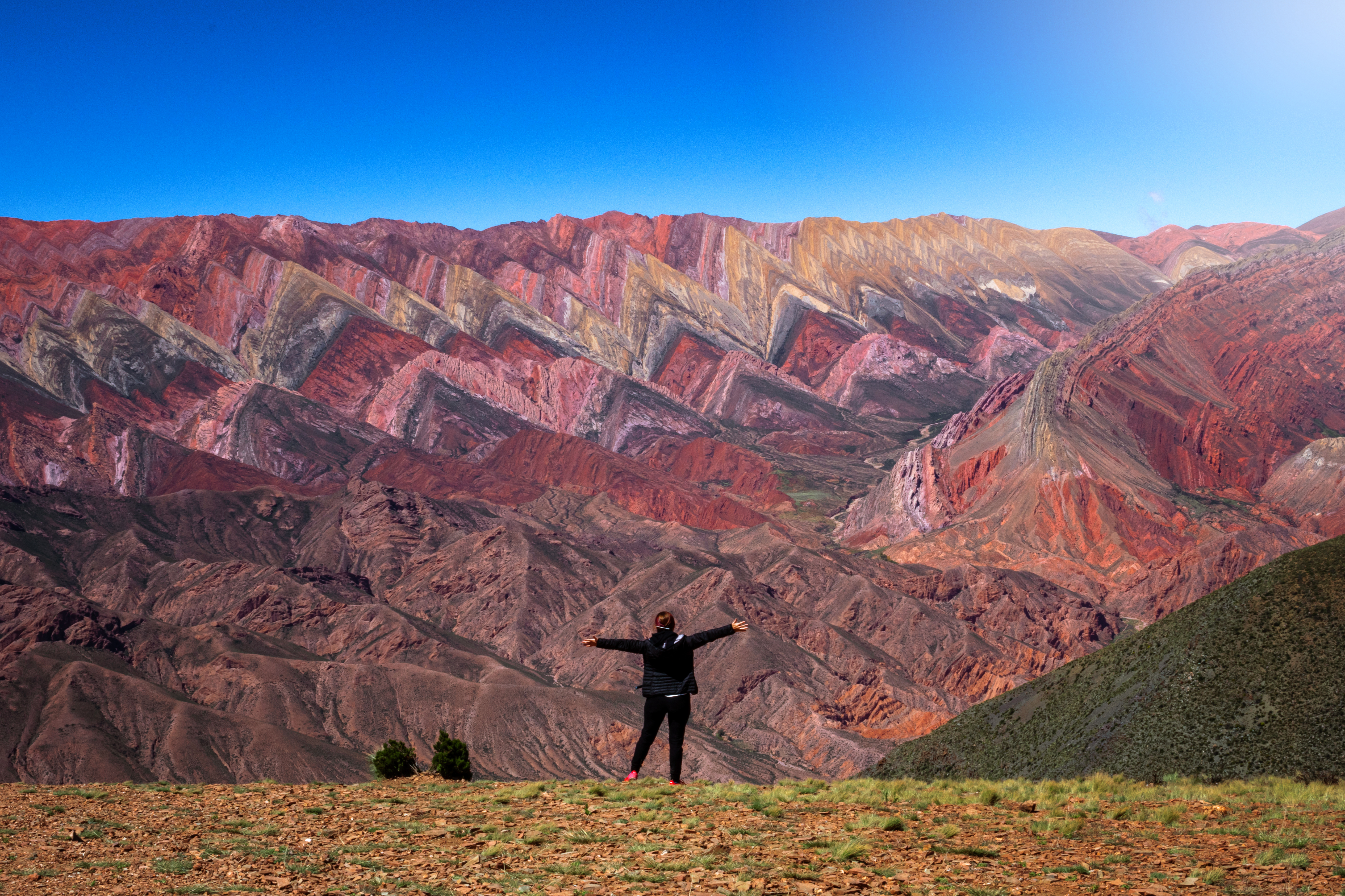 A happy person standing in front of the colorful mountains of El Hornocal, Argentina